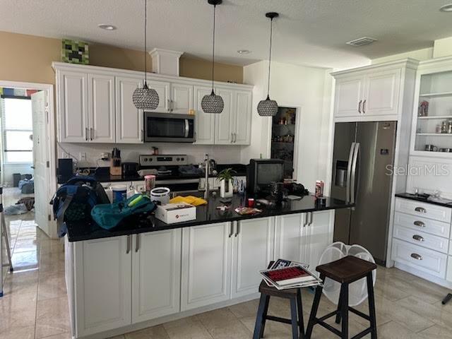 A kitchen features white cabinetry, black countertops, a central island, and three pendant lights — 5040 NE 48TH COURT, HIGH SPRINGS, FL