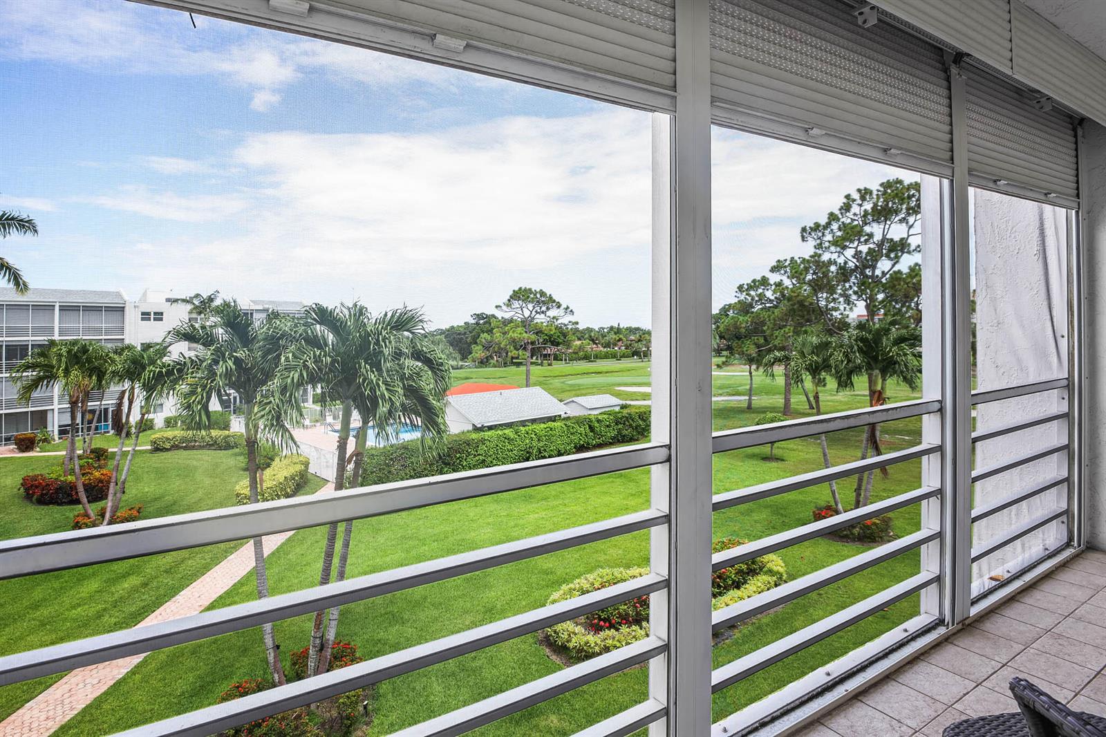 A screened balcony overlooks a green lawn, palm trees, and a distant golf course — 6850 10th Avenue N # 313, FL 33467, FL