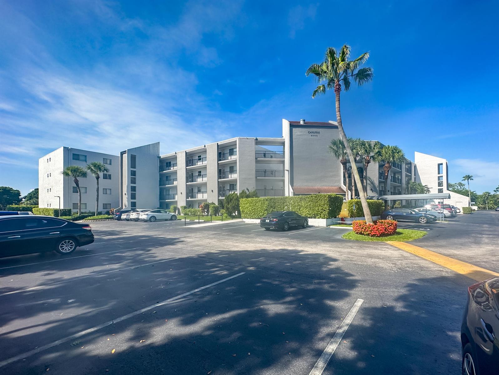 A multi-story apartment building with a parking lot and palm trees under a blue sky — 6850 10th Avenue N # 313, FL 33467, FL