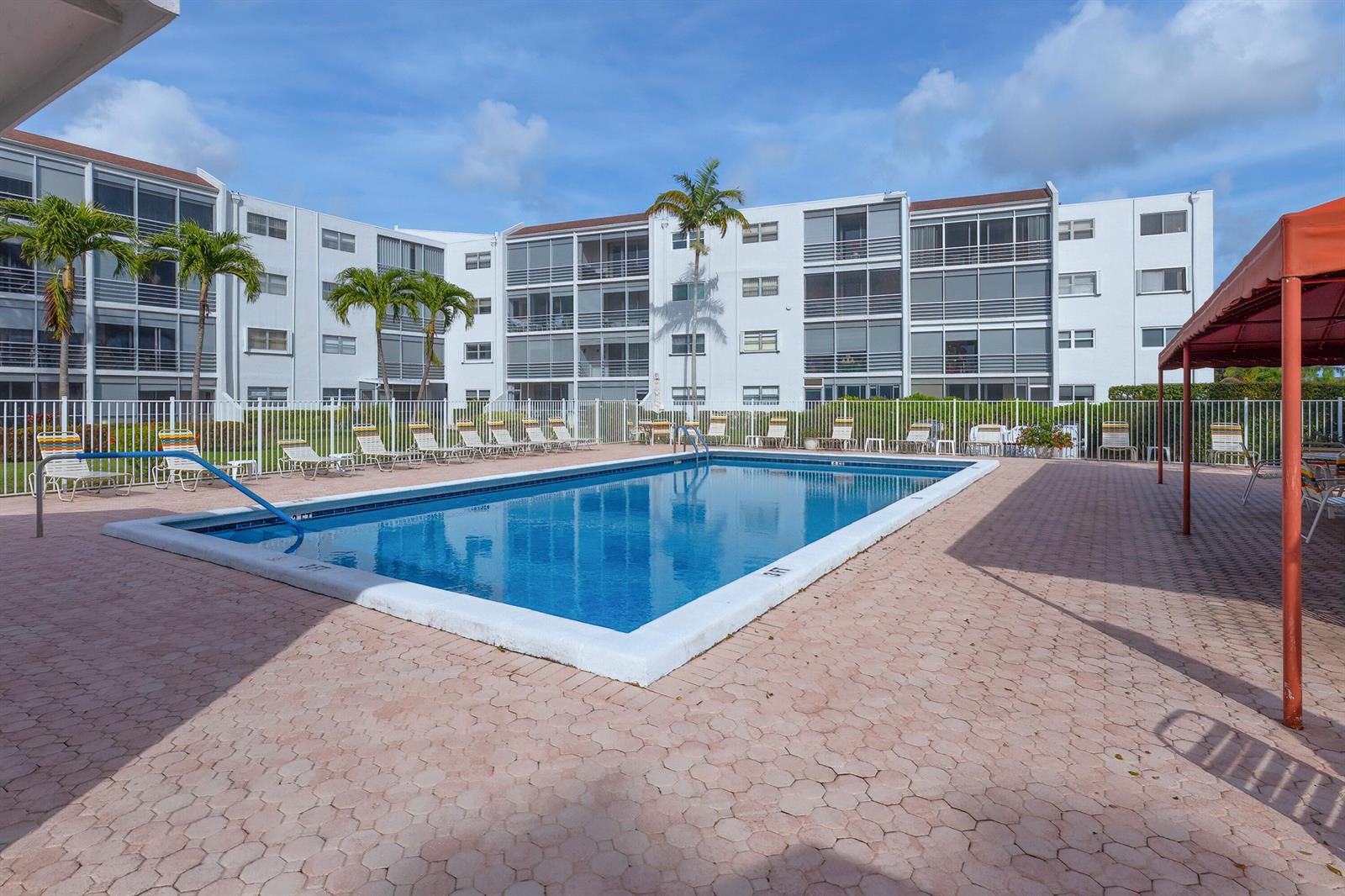 A rectangular swimming pool sits on a paved patio in front of a multi-story apartment building — 6850 10th Avenue N # 313, FL 33467, FL