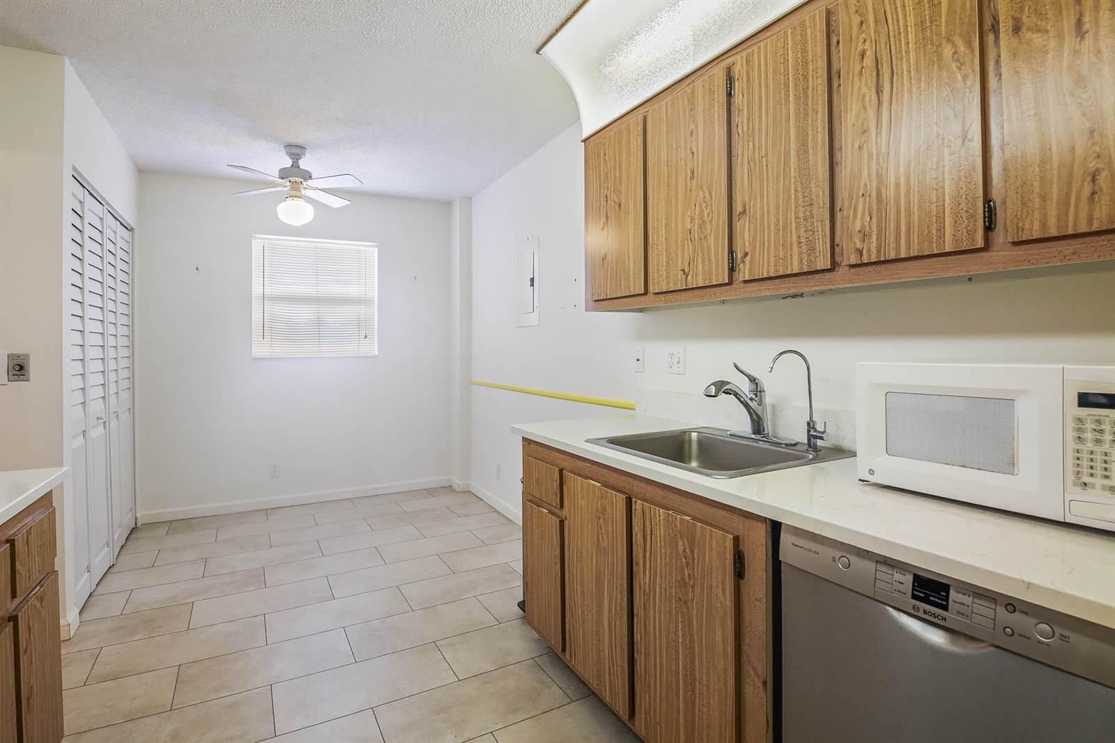 A kitchen with wood cabinets, a stainless steel sink, a dishwasher, and tile flooring — 6850 10th Avenue N # 313, FL 33467, FL