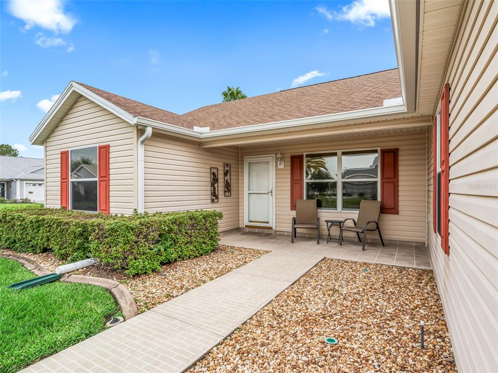 A beige house exterior features a covered porch, red shutters, and a stone walkway — 1502 AQUINO LANE, THE VILLAGES, FL