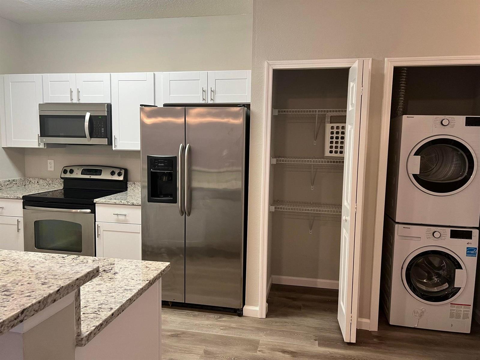 A kitchen features white cabinets, stainless steel appliances, granite countertops, a pantry, and stacked laundry — 4998 Key Lime Drive # 105, Jacksonville FL 32256, JACKSONVILLE, FL