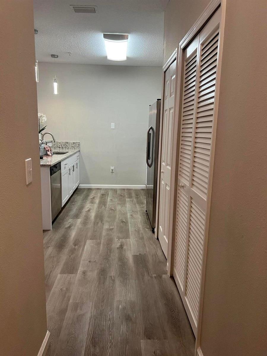 A galley-style kitchen features white cabinets, granite countertops, stainless steel appliances, and wood-look flooring — 4998 Key Lime Drive # 105, Jacksonville FL 32256, JACKSONVILLE, FL