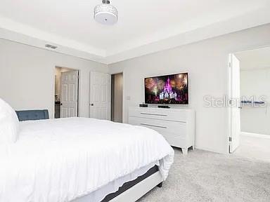 A bedroom features a white bed, a dresser with a television, and light-colored carpeting — 2182 FLEMING MIST PLACE, KISSIMMEE, FL