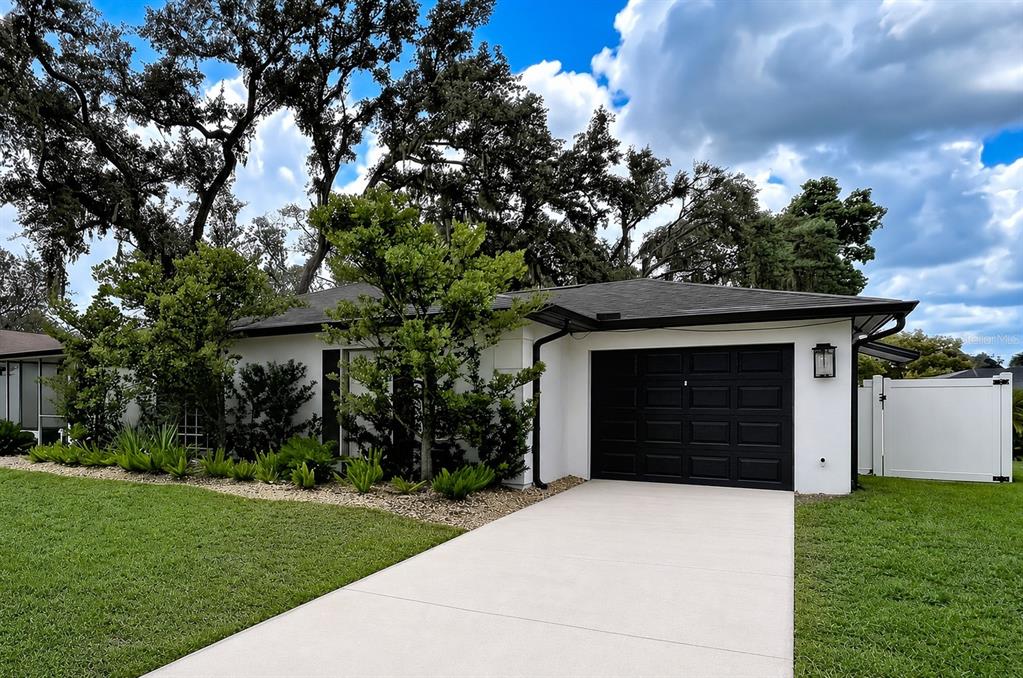 A white single-story house with a black garage door and landscaping under a cloudy sky — 1005 HALLWOOD LOOP, BRANDON, FL