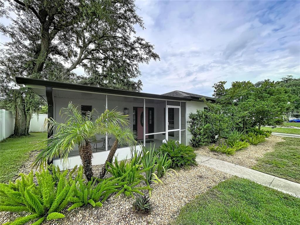A single-story house features a screened-in front porch, a pink door, and landscaped gravel beds — 1005 HALLWOOD LOOP, BRANDON, FL