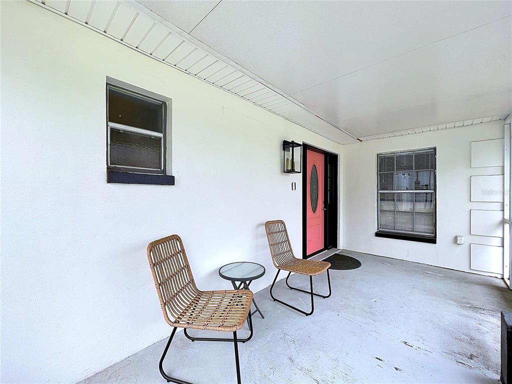 A covered patio features white walls, a pink front door, and two wicker chairs — 1005 HALLWOOD LOOP, BRANDON, FL