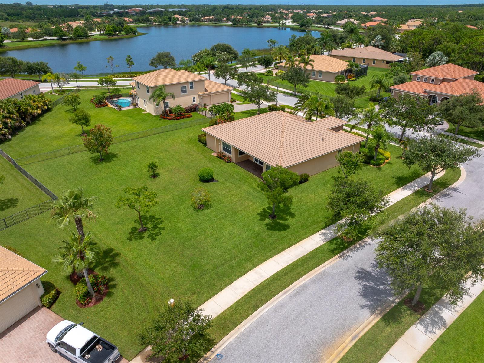 An aerial view of a suburban neighborhood featuring single-family homes, manicured lawns, and a lake — 7422 SE Belle Maison Drive, Stuart FL 34997, STUART, FL
