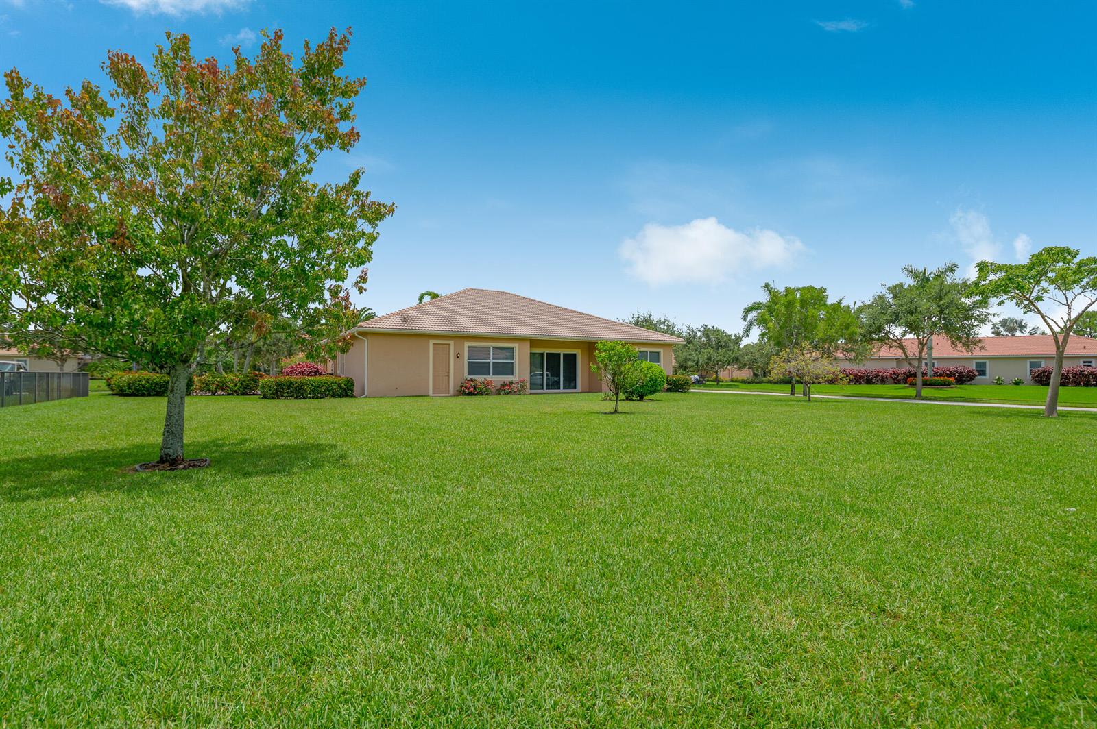 A single-story house with a tan exterior and a tiled roof sits on a grassy lawn — 7422 SE Belle Maison Drive, Stuart FL 34997, STUART, FL