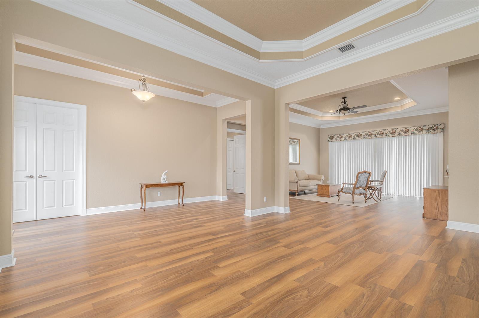A spacious living area features light-colored walls, wood-look flooring, and recessed tray ceilings — 7422 SE Belle Maison Drive, Stuart FL 34997, STUART, FL