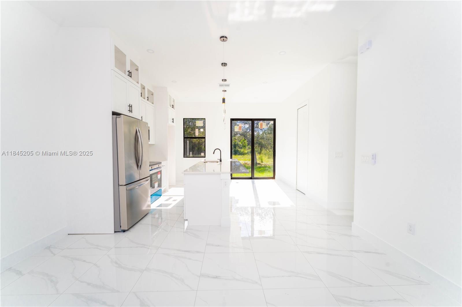 A modern kitchen features white cabinetry, stainless steel appliances, a center island, and marble-look flooring — 919 Glenn Ave, Lehigh Acres FL 33972, LEHIGH ACRES, FL