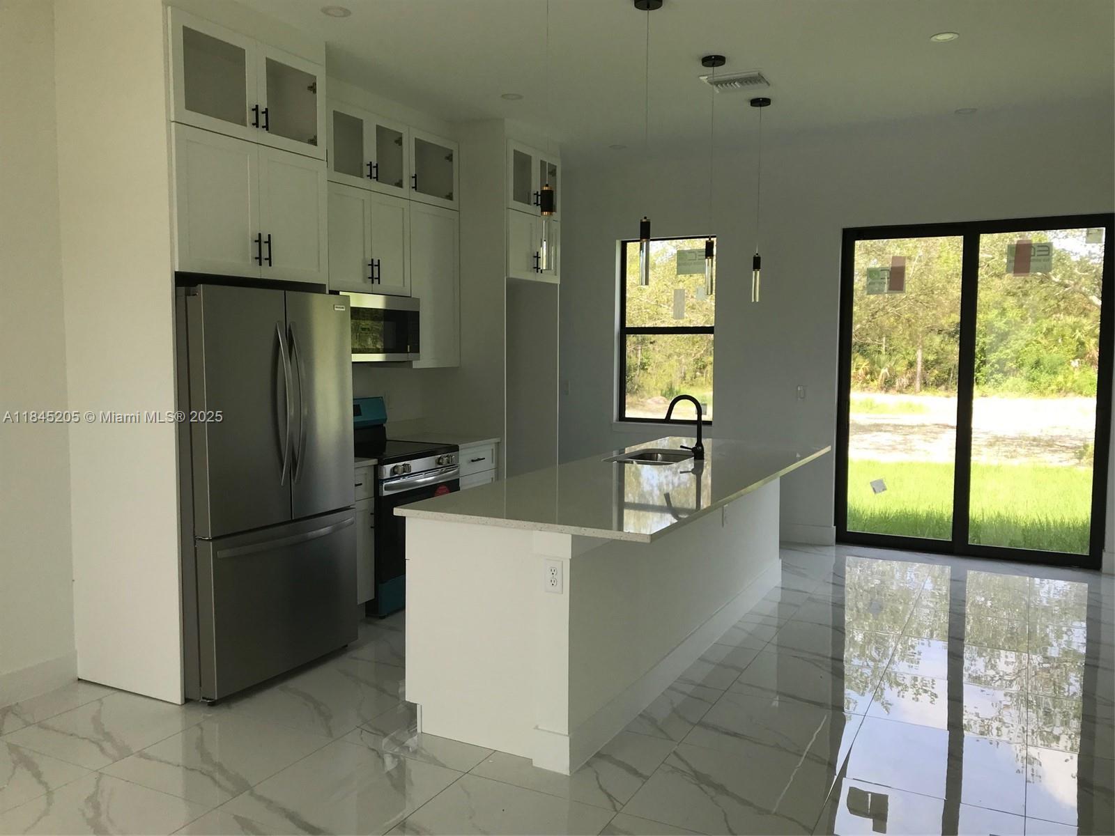 A modern kitchen features white cabinetry, stainless steel appliances, a quartz island, and tile flooring — 919 Glenn Ave, Lehigh Acres FL 33972, LEHIGH ACRES, FL