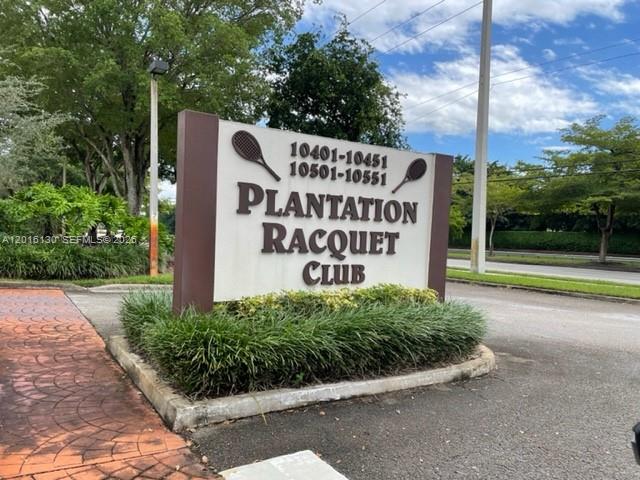 A sign for the Plantation Racquet Club stands in a landscaped area near a road — PLANTATION, FL