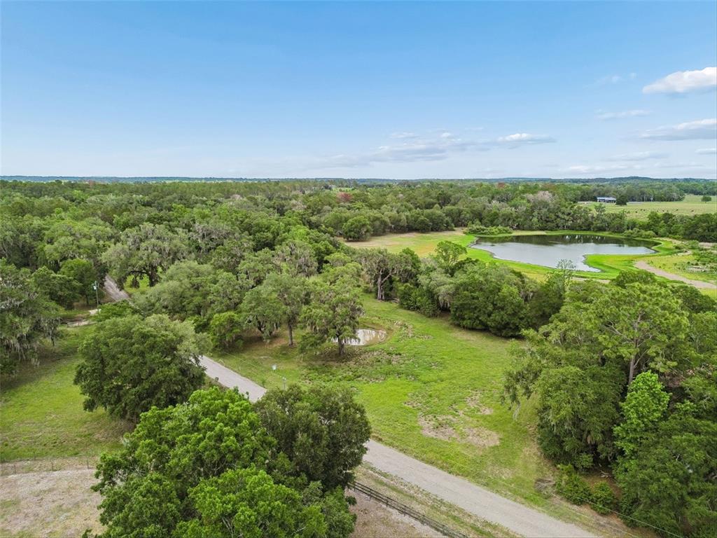 An aerial view shows a dirt road winding through a grassy, tree-filled rural landscape — 000 PALOMINO LAKES DR, DADE CITY, FL