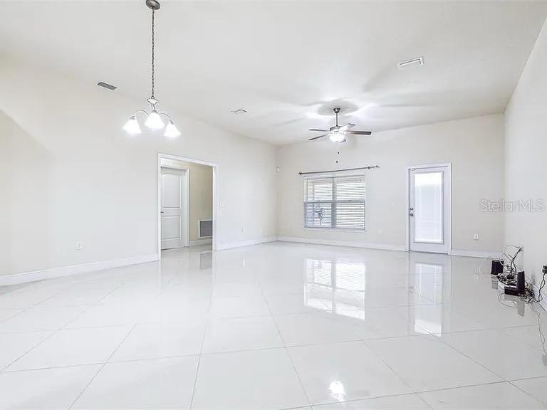 A spacious room with white tile floors, a ceiling fan, and a hanging light fixture — 404 RIO GRANDE COURT, POINCIANA, FL