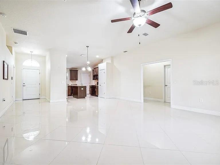 A bright, open-concept living area features white tile flooring, a ceiling fan, and a kitchen — 404 RIO GRANDE COURT, POINCIANA, FL