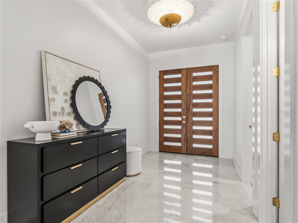 A modern entryway features a black dresser, a round mirror, and double wooden front doors — 1821 ENGLEWOOD ROAD, WINTER PARK, FL