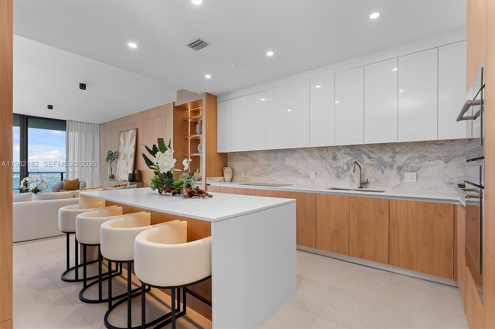 A modern kitchen features a white island, light wood cabinetry, and a marble backsplash — 700 NE 24rd St # 5802, Miami FL 33137, MIAMI, FL