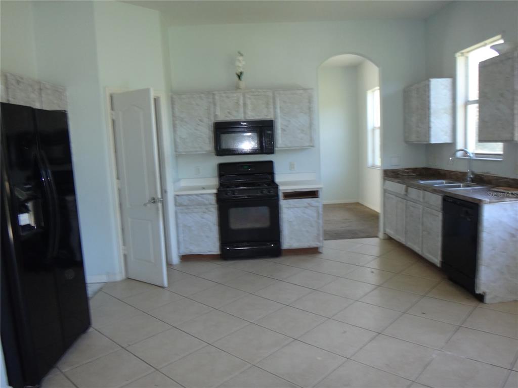 A kitchen features light-colored faux-marble cabinets, black appliances, and beige tile flooring — 19939 TAMIAMI AVENUE, TAMPA, FL