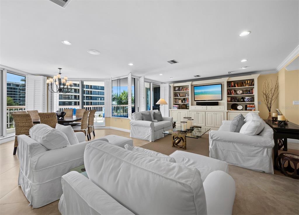 A bright living and dining area features white slipcovered furniture, built-in shelving, and balcony access — 455 LONGBOAT CLUB ROAD UNIT 402, LONGBOAT KEY, FL