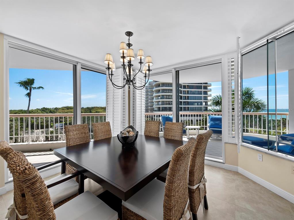 A dining room with a dark wood table, wicker chairs, and floor-to-ceiling windows overlooking balconies — 455 LONGBOAT CLUB ROAD UNIT 402, LONGBOAT KEY, FL