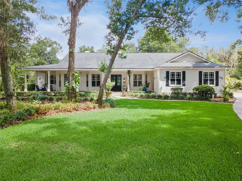 A single-story white house with a covered porch and black shutters sits behind a lawn — 5002 MUIR WAY, LITHIA, FL