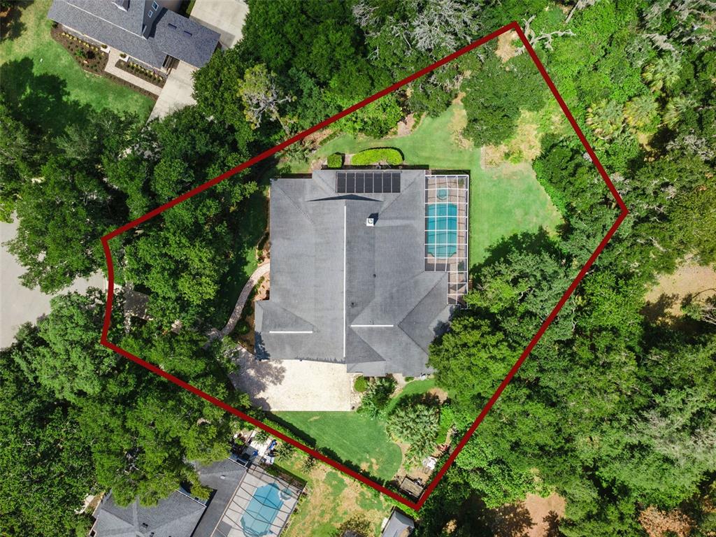 An aerial view shows a house with a pool and solar panels on a wooded lot — 5002 MUIR WAY, LITHIA, FL