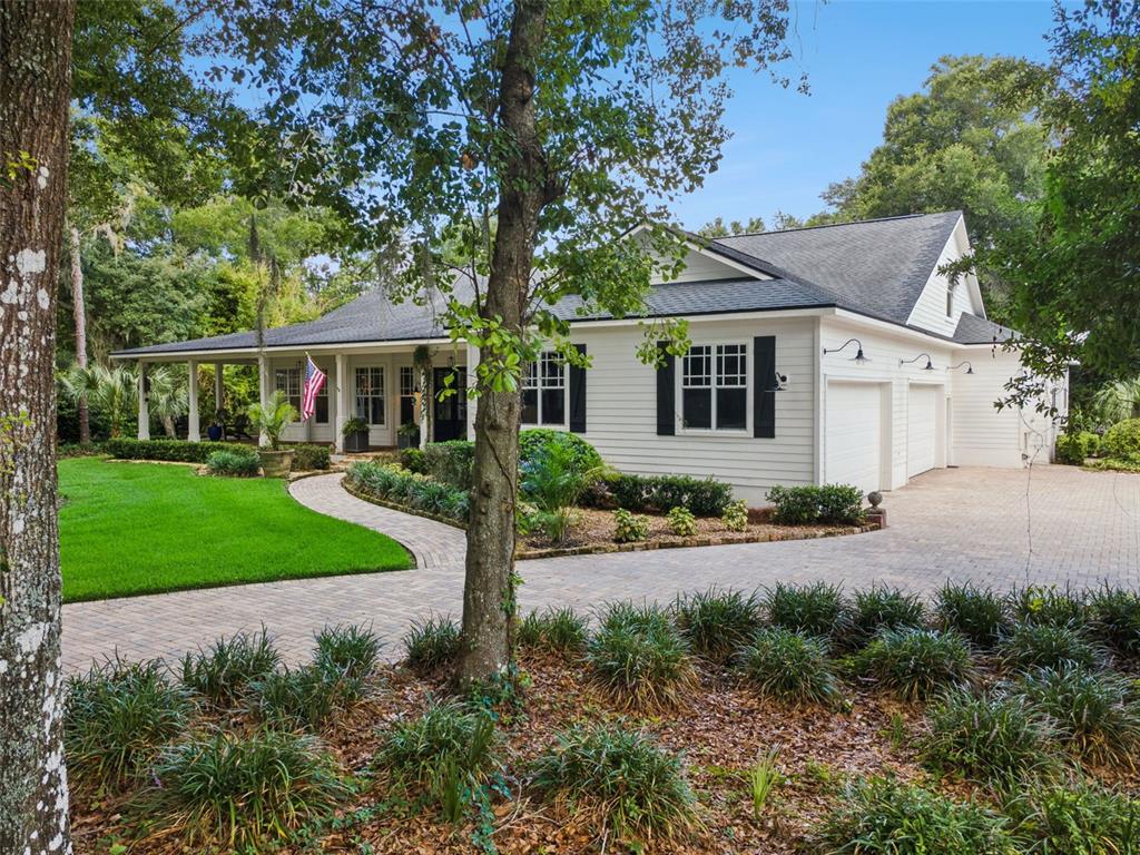 A white house with black shutters and a brick driveway sits among mature trees — 5002 MUIR WAY, LITHIA, FL
