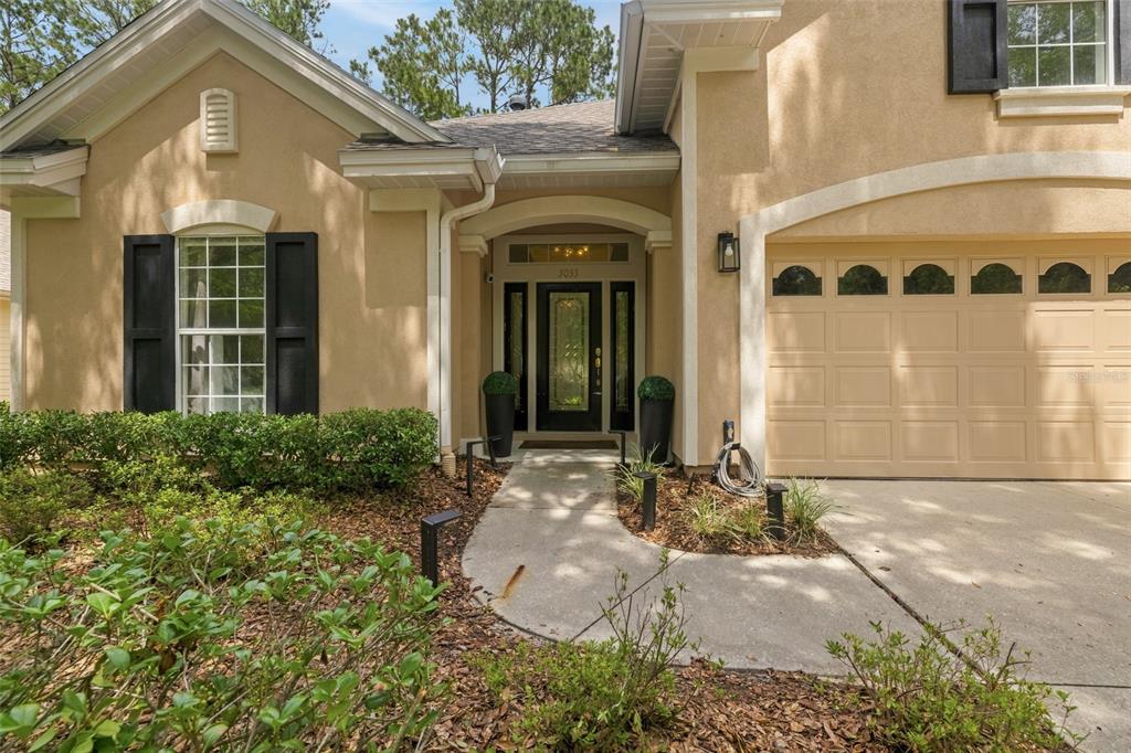 A tan stucco house exterior features a front door, a garage, and a concrete walkway — 3033 SW 98TH DRIVE, GAINESVILLE, FL