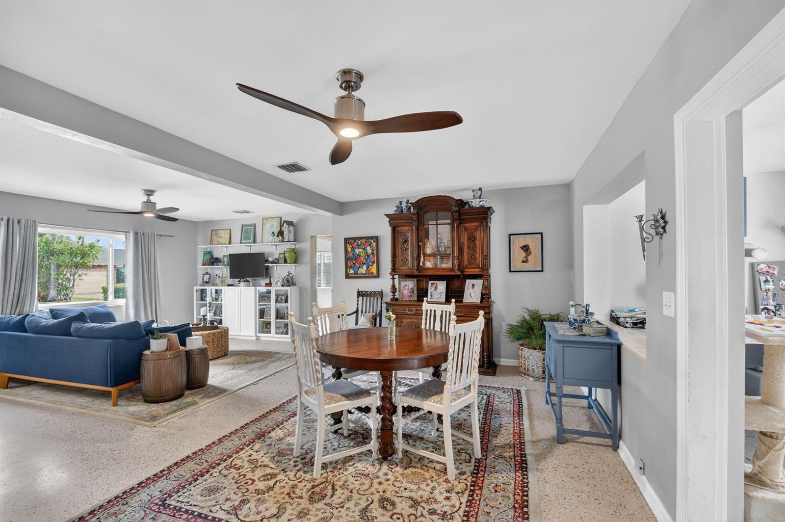 An open-concept dining and living area features a wooden hutch, round table, and blue sofa — 338 Edmor Road, West Palm Beach FL 33405, WEST PALM BEACH, FL