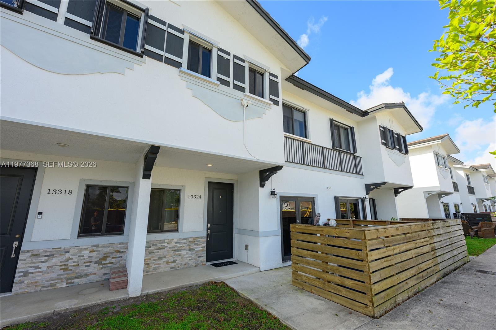 The exterior of a two-story townhouse features white stucco walls, dark shutters, and a wooden fence — 13324 SW 250th St, Miami FL 33032, MIAMI, FL