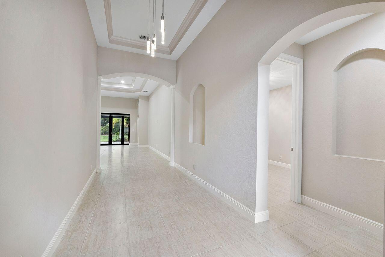 A bright hallway with light tile flooring, arched doorways, and a modern pendant light fixture — 8231 Canopy Terrace, Parkland FL 33076, PARKLAND, FL