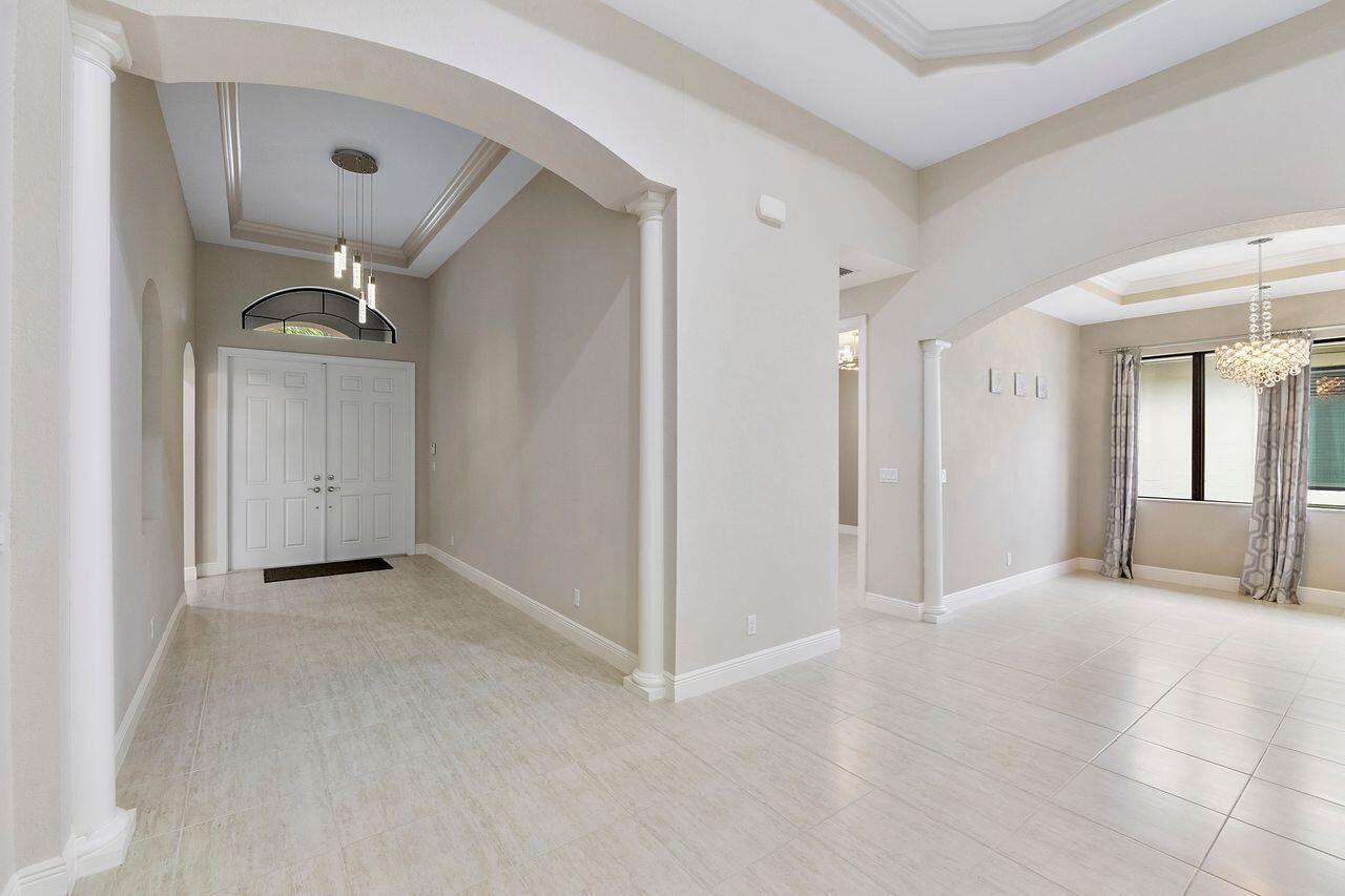 A bright foyer with tile floors, arched entryways, white columns, and a modern chandelier — 8231 Canopy Terrace, Parkland FL 33076, PARKLAND, FL