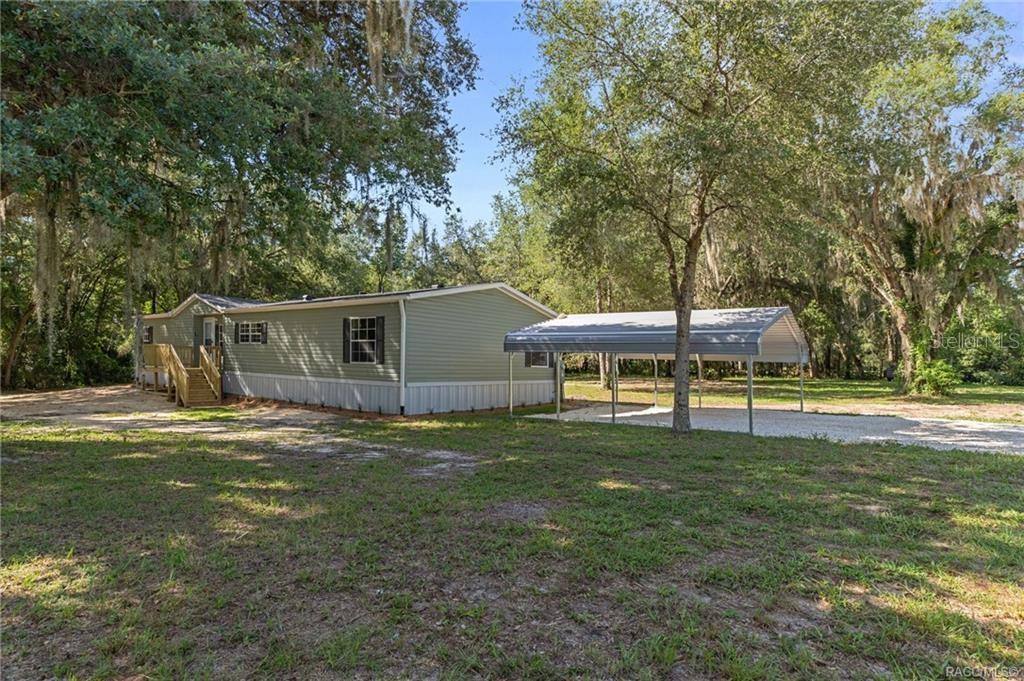 A mobile home with a wooden deck and a metal carport sits on a grassy lot — 11437 N YOUNG DRIVE, DUNNELLON, FL