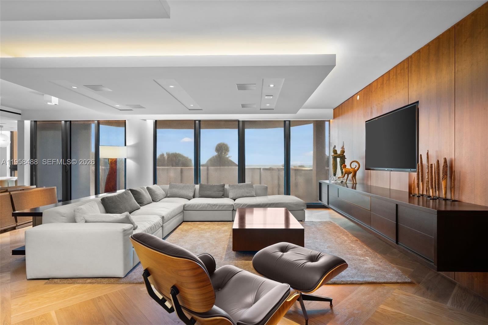 A modern living room features a large sectional sofa, wood paneling, and floor-to-ceiling windows — 9999 Collins Ave # 3E, Bal Harbour FL 33154, BAL HARBOUR, FL
