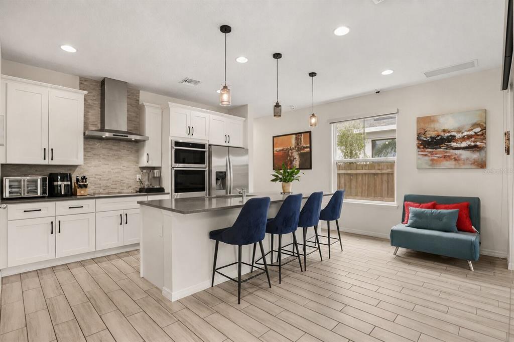 A modern kitchen features white cabinetry, a gray island with blue barstools, and tile flooring — 2338 S BROWN AVENUE, ORLANDO, FL