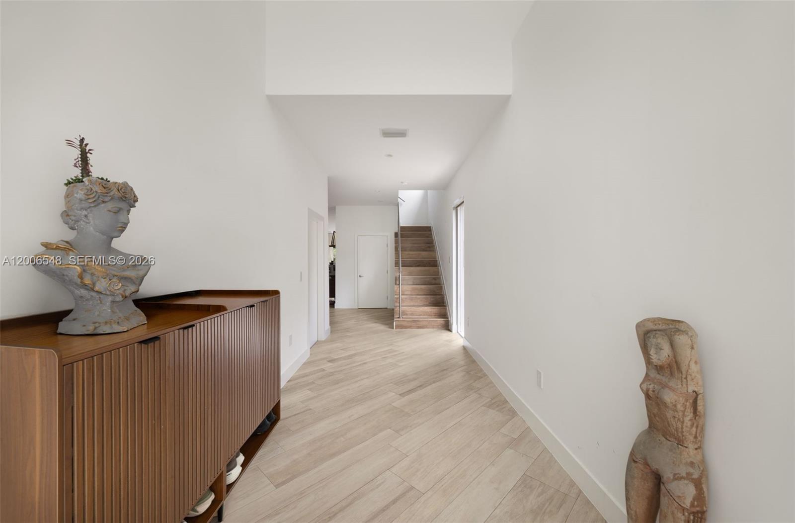A modern hallway features light wood-look flooring, white walls, a wooden cabinet, and two sculptures — 2931 SW 27th Ter # 2931, Miami FL 33133, MIAMI, FL