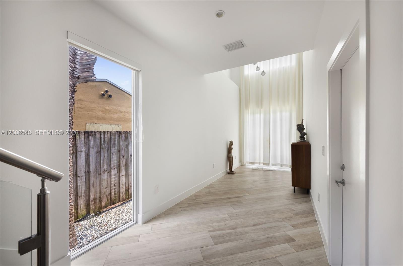 A bright hallway features light wood-look tile flooring, a tall window, and a glass railing — 2931 SW 27th Ter # 2931, Miami FL 33133, MIAMI, FL