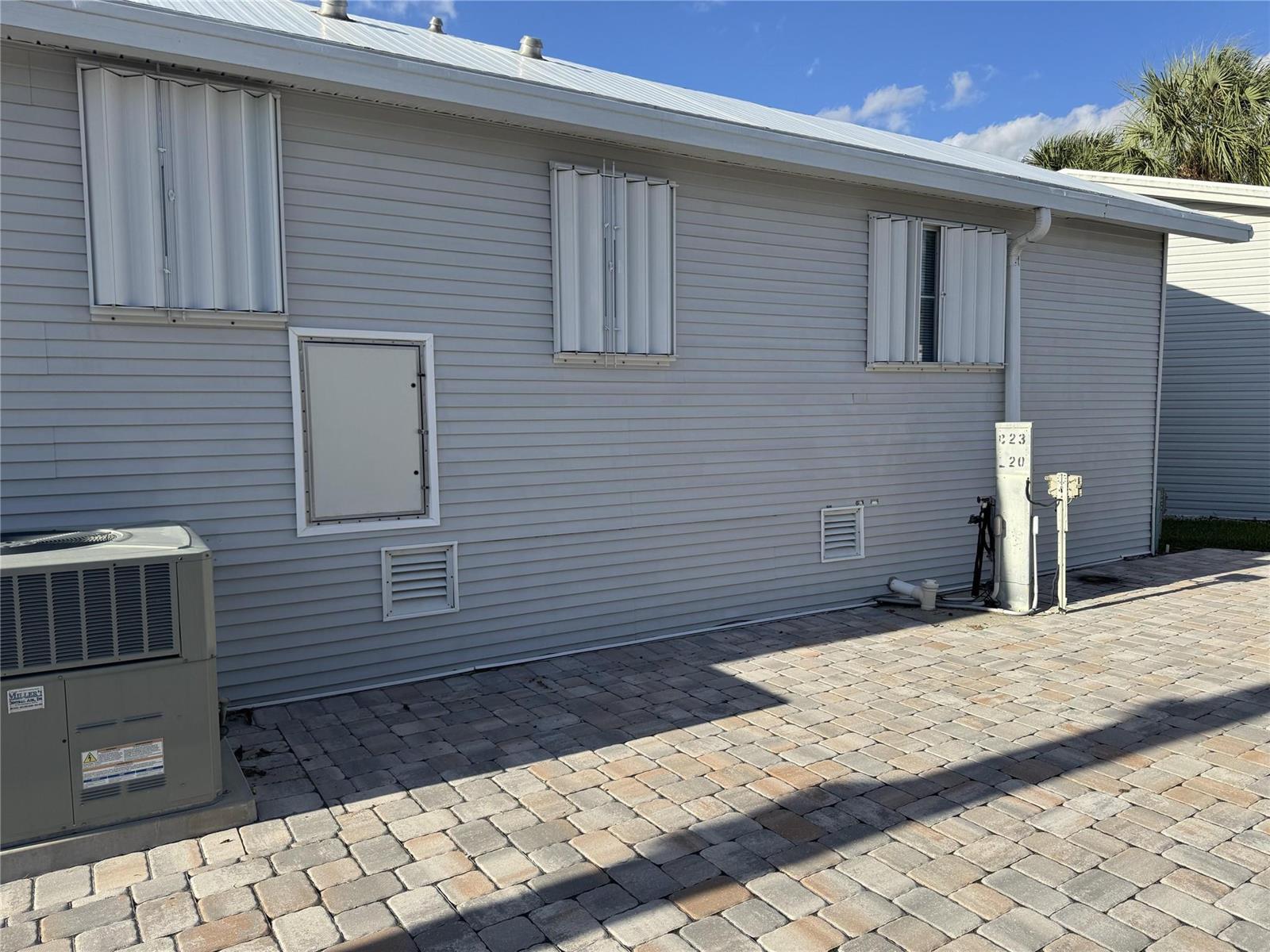 The exterior of a light gray house features white accordion shutters and a paved patio — 6475 52nd Street, Okeechobee FL 34974, OKEECHOBEE, FL