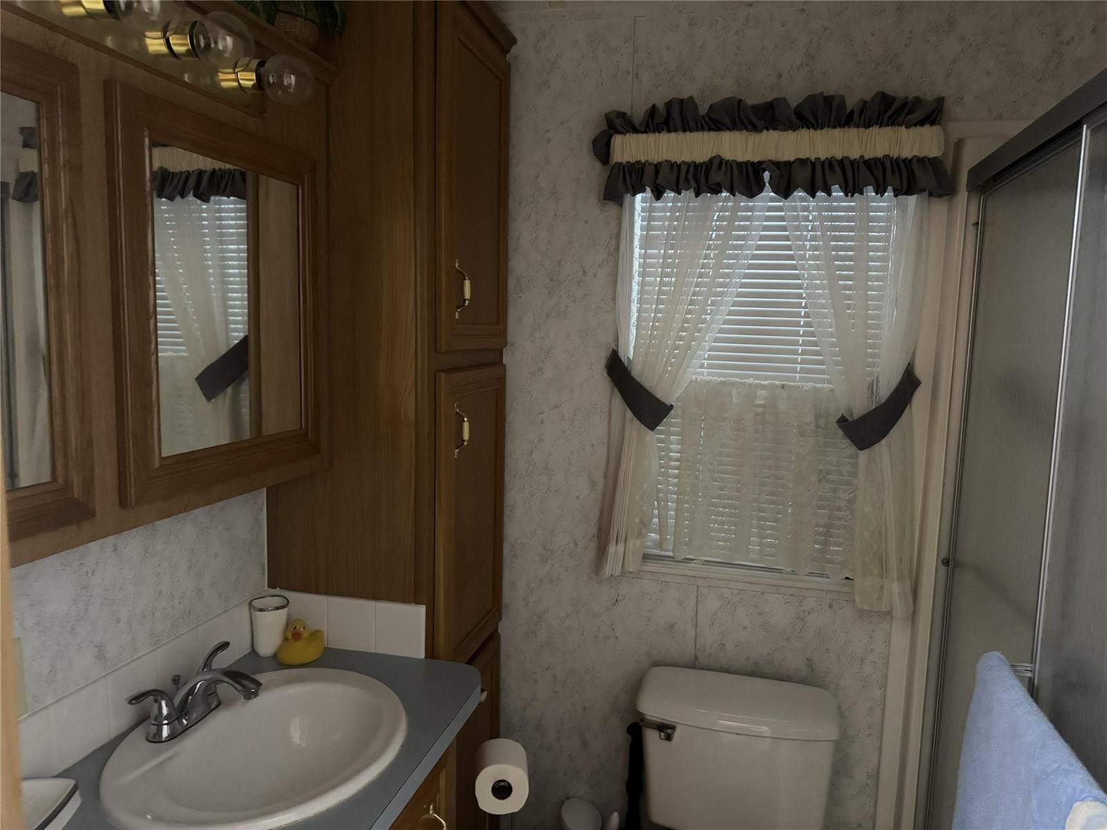 A bathroom features a vanity with a sink, wooden cabinetry, a toilet, and a window — 6475 52nd Street, Okeechobee FL 34974, OKEECHOBEE, FL