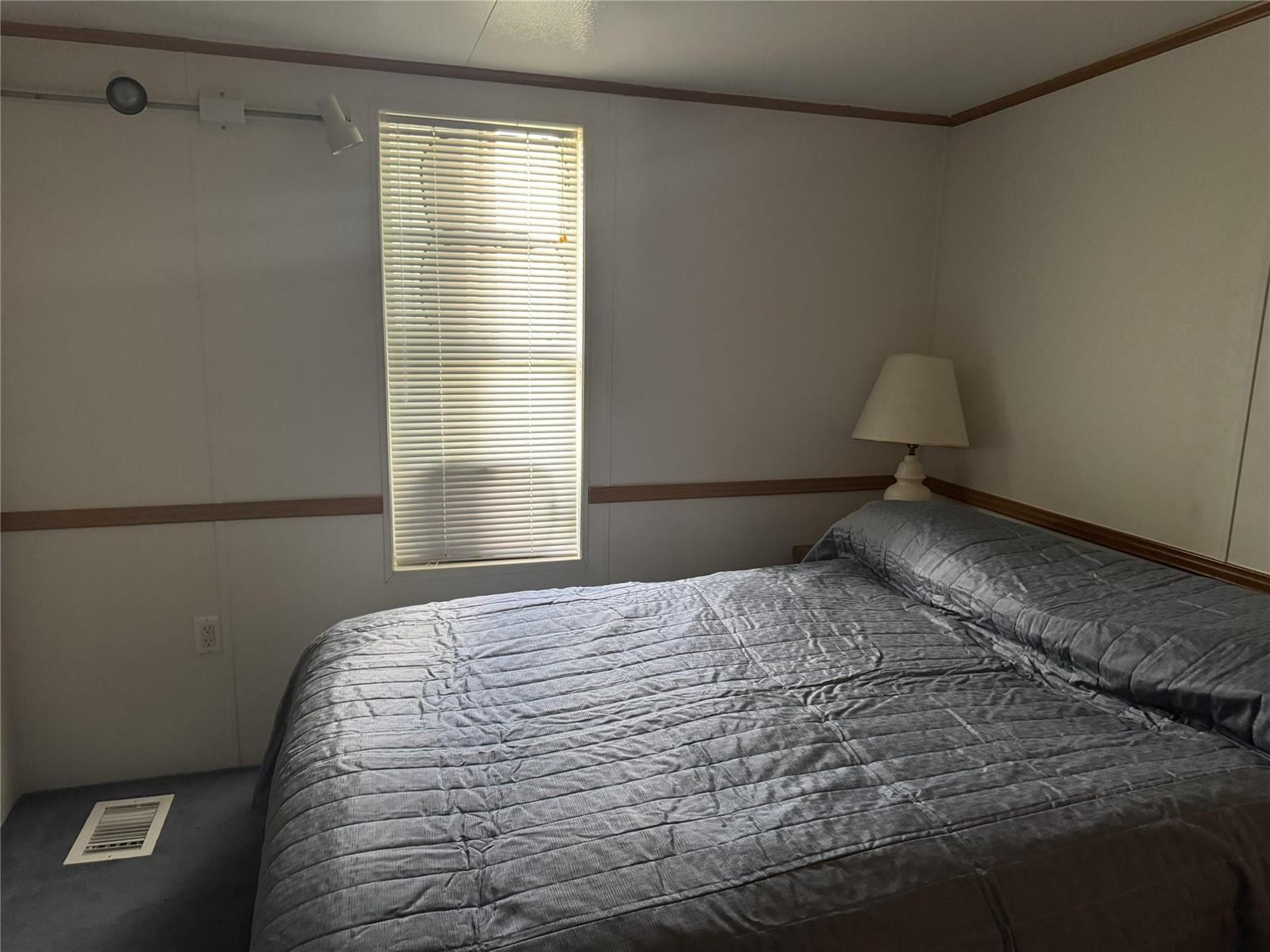 A bedroom features a bed with a grey quilt, a window with blinds, and wall-mounted lighting — 6475 52nd Street, Okeechobee FL 34974, OKEECHOBEE, FL