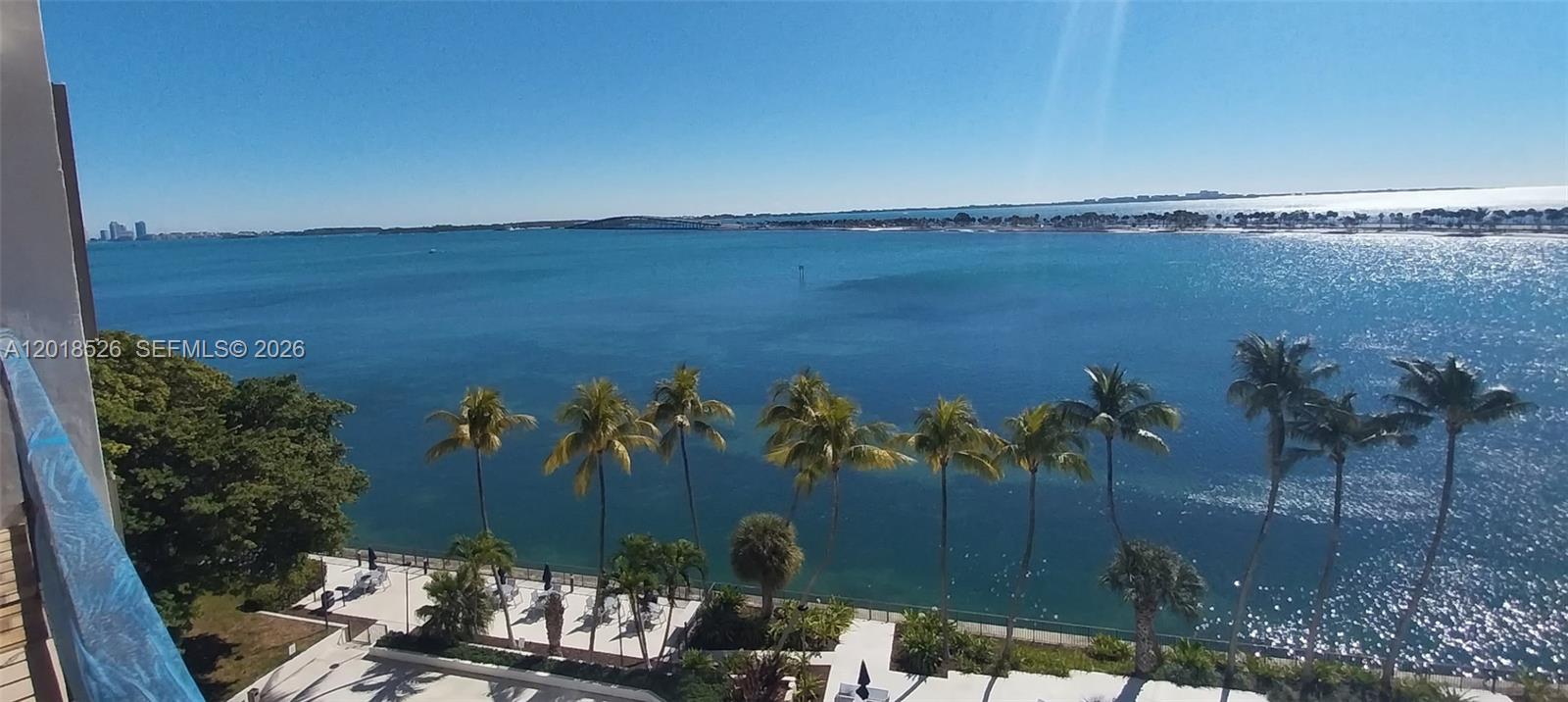 A high-angle view shows a waterfront balcony overlooking palm trees, a pool area, and bay — 2333 Brickell Ave # 602, Miami FL 33129, MIAMI, FL