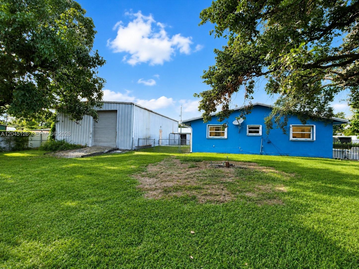A blue house and a metal warehouse stand on a grassy lot under trees — 6145 Hayes St, Hollywood FL 33024, HOLLYWOOD, FL