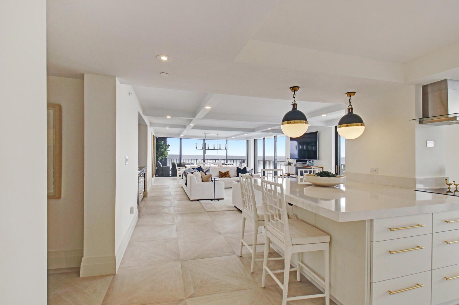 A modern kitchen island with bar stools overlooks an open-concept living area with ocean views — 400 Beach Road # 504, Tequesta FL 33469, TEQUESTA, FL