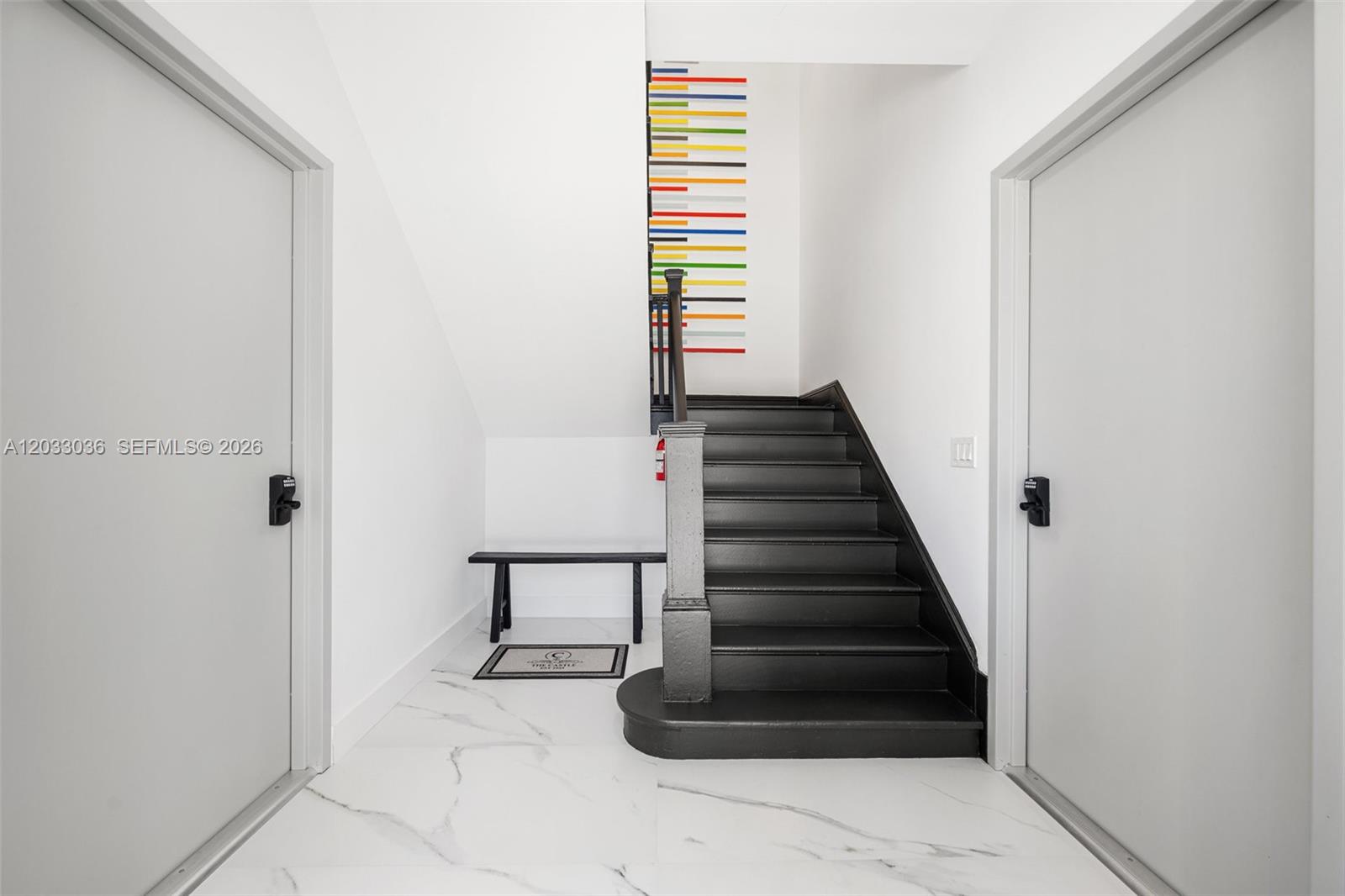 A white hallway features a black staircase, a small bench, and colorful wall art — 403 SW 12th Ave # 3, Miami FL 33130, MIAMI, FL
