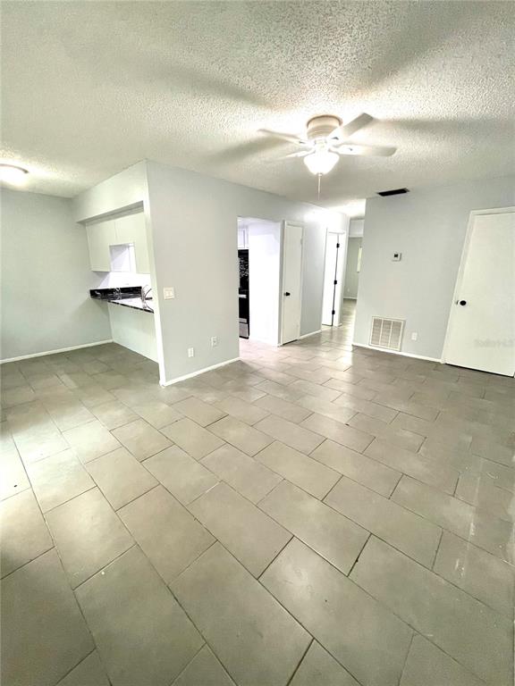 A living area with gray tile flooring, a ceiling fan, and an open kitchen pass-through — 3767 138TH AVENUE UNIT B, LARGO, FL