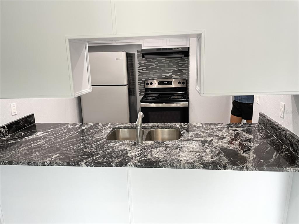 A kitchen features a black and white granite countertop, stainless steel sink, and black appliances — 3767 138TH AVENUE UNIT B, LARGO, FL