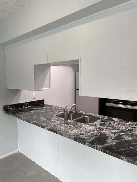 A kitchen features white cabinets, a black and white granite countertop, and a stainless sink — 3767 138TH AVENUE UNIT B, LARGO, FL