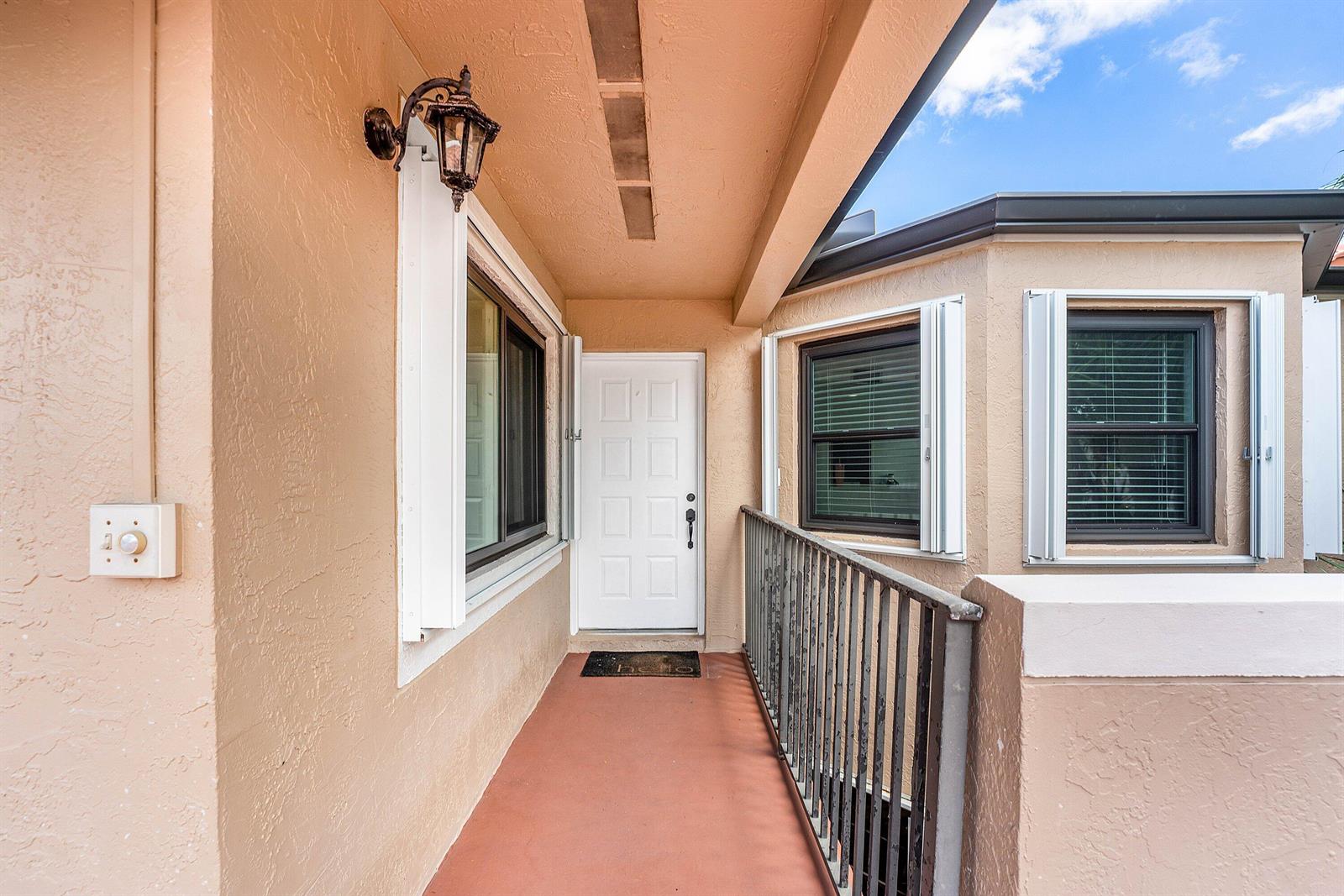 An exterior view of a covered entryway with a white door and metal railing — 6614 Villa Sonrisa Drive # 123, Boca Raton FL 33433, BOCA RATON, FL